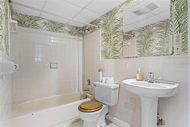 bathroom with tile walls, tiled shower / bath, toilet, and a drop ceiling