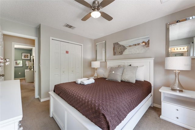 bedroom with light carpet, ceiling fan, a closet, and a textured ceiling