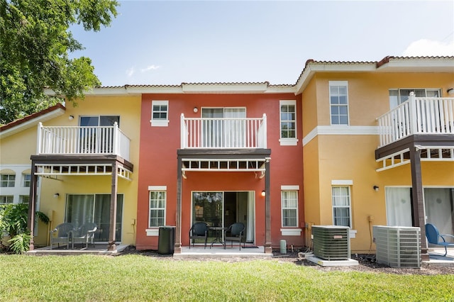 rear view of property with a yard, central AC, a balcony, and a patio area