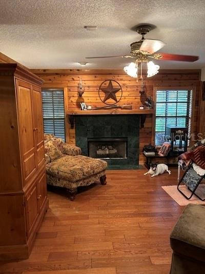 living area with ceiling fan, wood-type flooring, wooden walls, and a textured ceiling