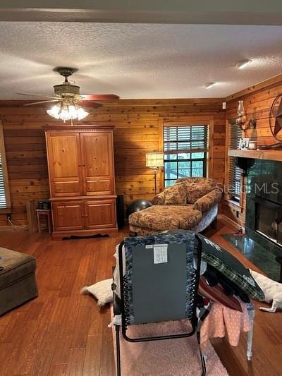 living room with ceiling fan, hardwood / wood-style floors, a textured ceiling, and wooden walls