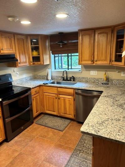 kitchen featuring range hood, sink, double oven range, stainless steel dishwasher, and a textured ceiling