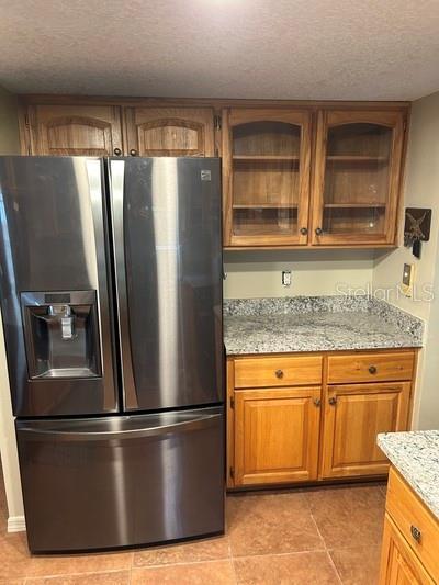 kitchen with light stone counters, stainless steel fridge, a textured ceiling, and light tile patterned floors