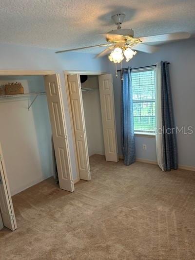 unfurnished bedroom featuring light carpet, ceiling fan, multiple closets, and a textured ceiling