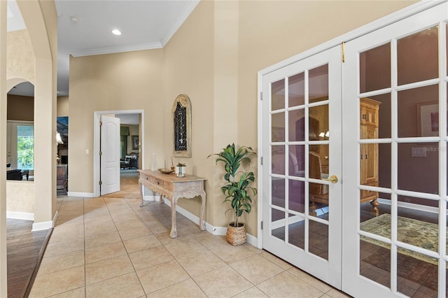 interior space with crown molding, a towering ceiling, light tile patterned flooring, and french doors