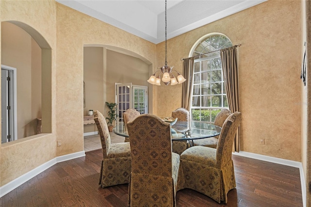 dining area featuring a towering ceiling, dark hardwood / wood-style flooring, and a notable chandelier