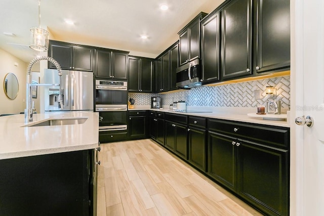 kitchen featuring sink, pendant lighting, stainless steel appliances, light hardwood / wood-style floors, and decorative backsplash