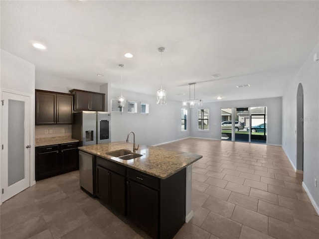 kitchen featuring sink, decorative light fixtures, appliances with stainless steel finishes, light stone countertops, and a kitchen island with sink