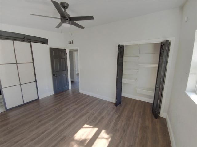 unfurnished bedroom featuring dark wood-type flooring, ceiling fan, a barn door, and a closet