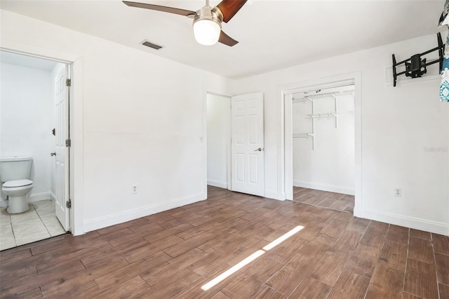 unfurnished bedroom featuring ensuite bath, dark wood-type flooring, a closet, and ceiling fan