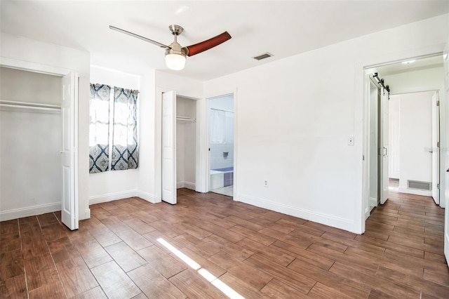 unfurnished bedroom with two closets, wood-type flooring, ceiling fan, and ensuite bathroom