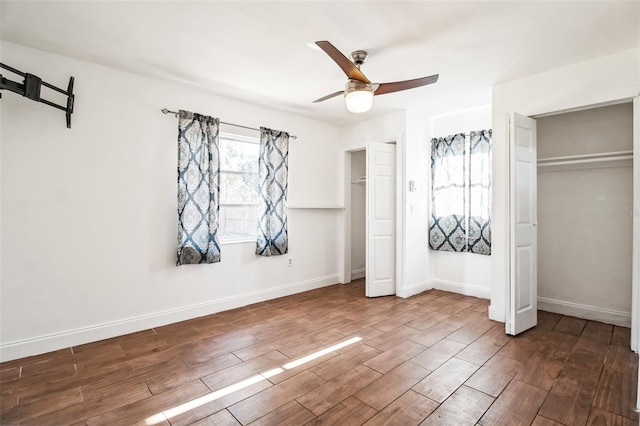 unfurnished bedroom featuring dark hardwood / wood-style flooring, ceiling fan, and multiple closets