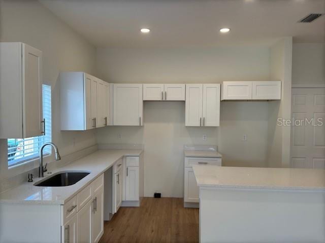 kitchen featuring a kitchen island, sink, white cabinets, light stone counters, and dark wood-type flooring