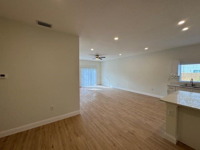 unfurnished living room with ceiling fan, sink, and light wood-type flooring