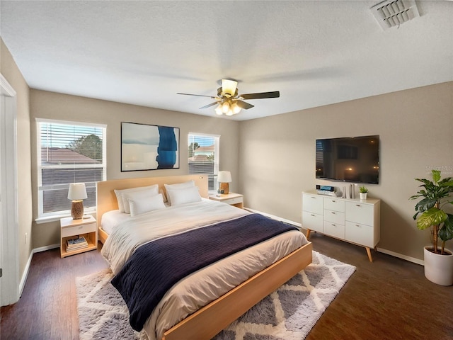 bedroom with ceiling fan, dark hardwood / wood-style floors, multiple windows, and a textured ceiling