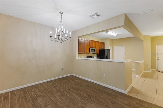 6912 Hochad Dr, Orlando, FL 32819 - kitchen featuring stainless steel microwave, black refrigerator with ice dispenser, a chandelier, wood finished floors, and brown cabinetry
