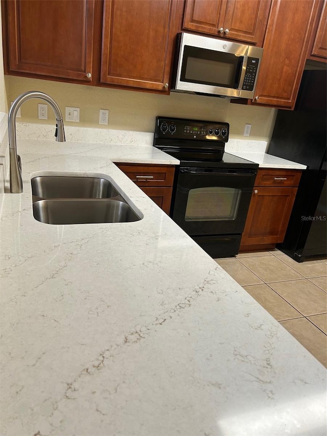 6912 Hochad Dr, Orlando, FL 32819 - kitchen with black appliances, light stone countertops, light tile patterned floors, and brown cabinetry