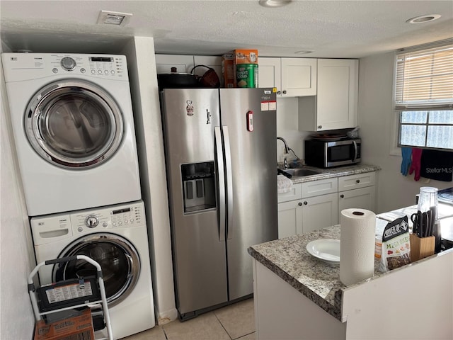 washroom with stacked washer / dryer, sink, light tile patterned floors, and a textured ceiling