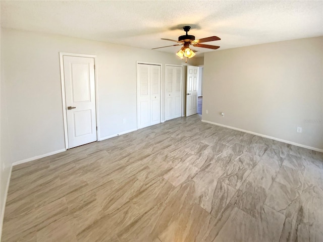 unfurnished bedroom with ceiling fan, a textured ceiling, and multiple closets