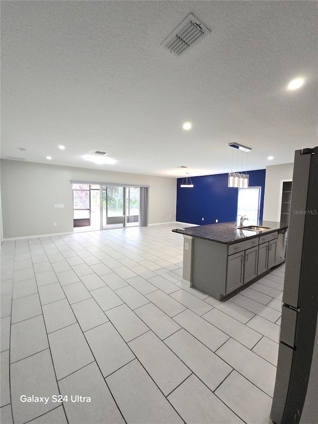 kitchen featuring a kitchen island with sink, light tile patterned floors, decorative light fixtures, and stainless steel fridge