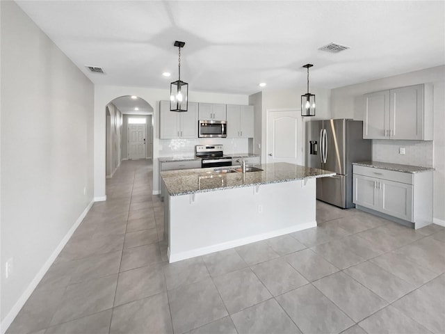 kitchen featuring sink, light stone counters, a center island with sink, stainless steel appliances, and backsplash