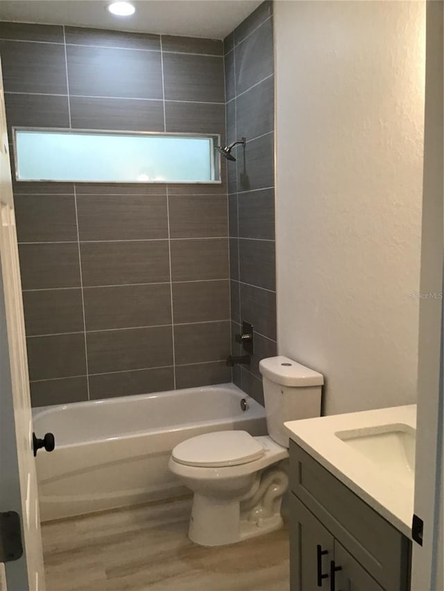 full bathroom with tiled shower / bath combo, vanity, hardwood / wood-style floors, and toilet