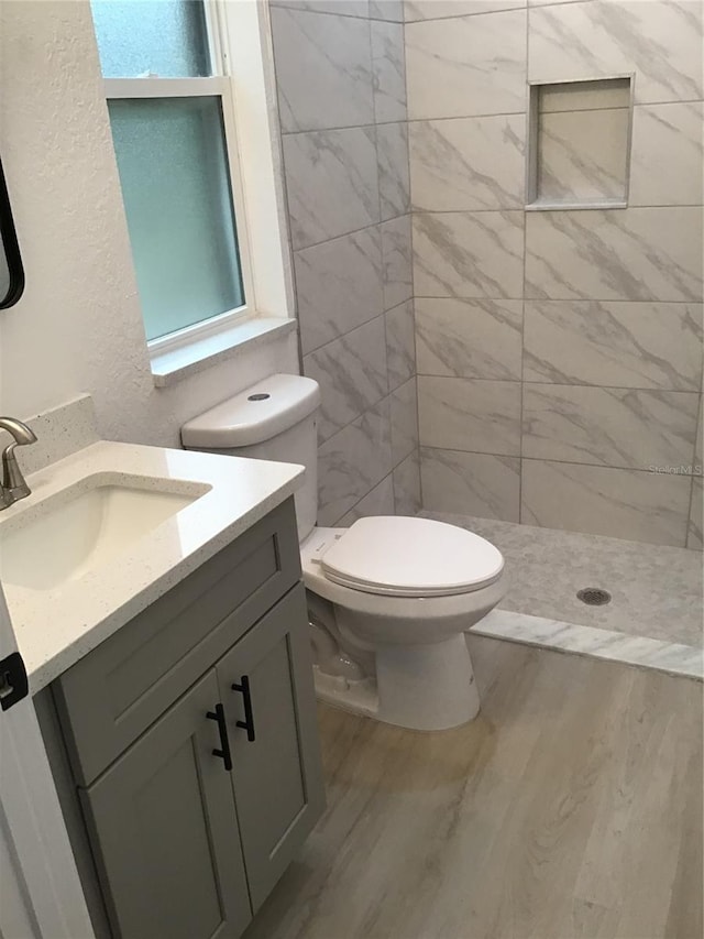 bathroom featuring vanity, wood-type flooring, toilet, and tiled shower