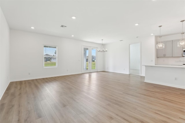 unfurnished living room featuring a healthy amount of sunlight, an inviting chandelier, and light wood-type flooring