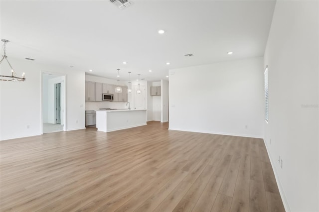 unfurnished living room with a chandelier and light wood-type flooring