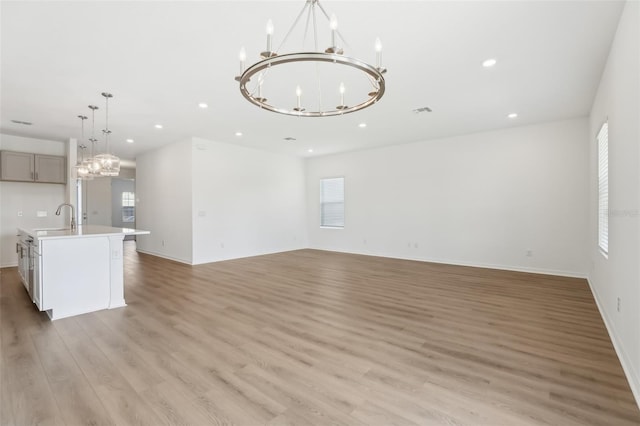 unfurnished living room featuring sink, an inviting chandelier, and light hardwood / wood-style floors