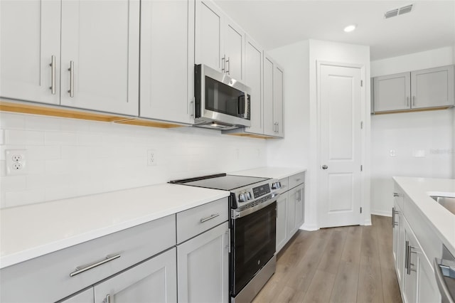 kitchen with appliances with stainless steel finishes, gray cabinets, decorative backsplash, and light hardwood / wood-style flooring