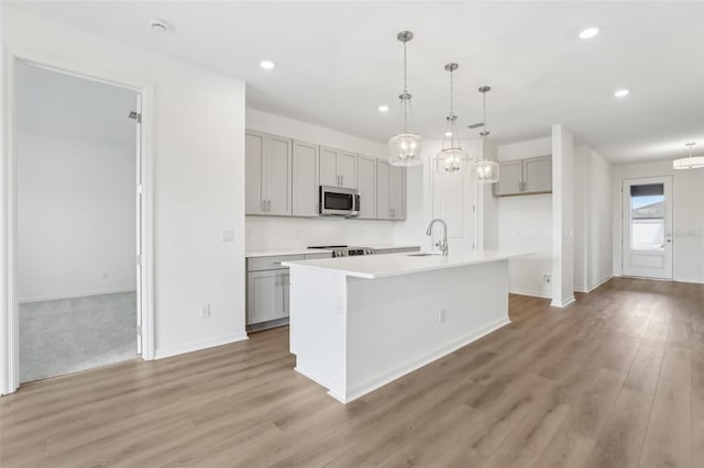 kitchen with sink, gray cabinets, a kitchen island with sink, hardwood / wood-style floors, and stainless steel appliances