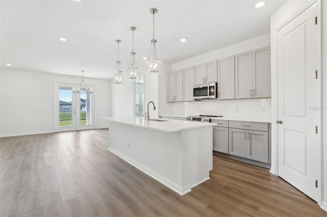 kitchen featuring sink, decorative light fixtures, gray cabinets, hardwood / wood-style flooring, and a kitchen island with sink