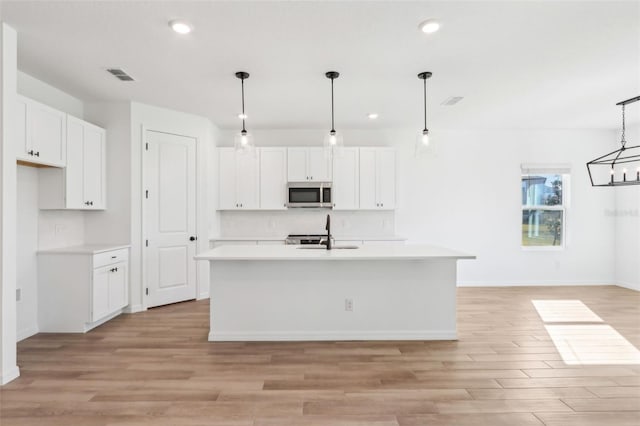 kitchen featuring white cabinets, visible vents, stainless steel microwave, and light countertops