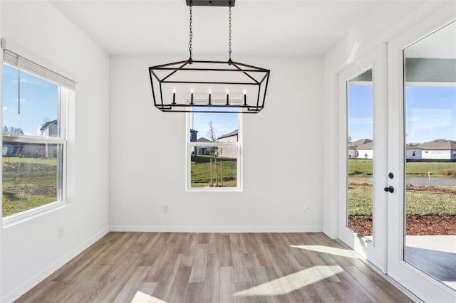 unfurnished dining area with light wood finished floors, french doors, and baseboards