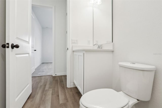 half bath featuring toilet, baseboards, wood finished floors, and vanity