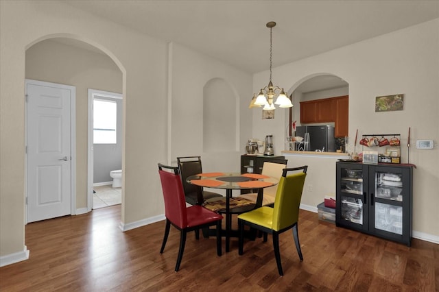 dining area featuring dark wood-style floors, a chandelier, arched walkways, and baseboards