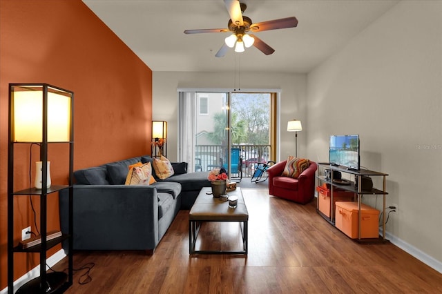 living room with dark wood-type flooring, a ceiling fan, and baseboards