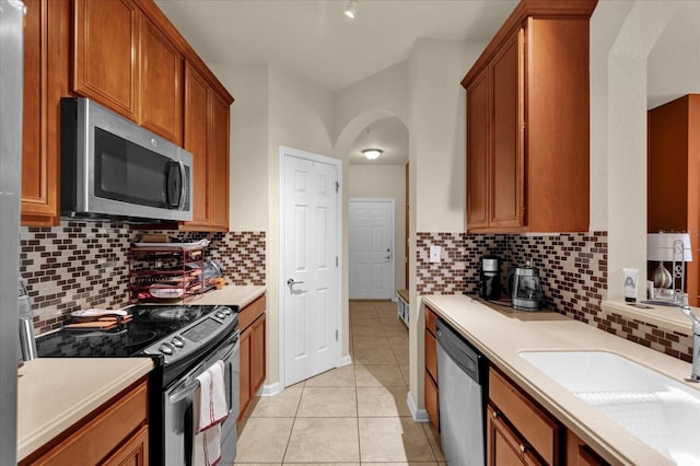 kitchen featuring a sink, light tile patterned floors, arched walkways, stainless steel appliances, and light countertops