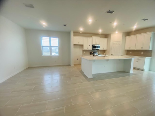 kitchen with light tile patterned floors, an island with sink, stainless steel appliances, decorative backsplash, and white cabinets