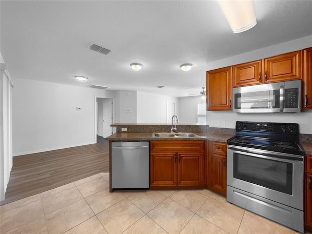 kitchen with light tile patterned flooring, sink, appliances with stainless steel finishes, kitchen peninsula, and dark stone counters