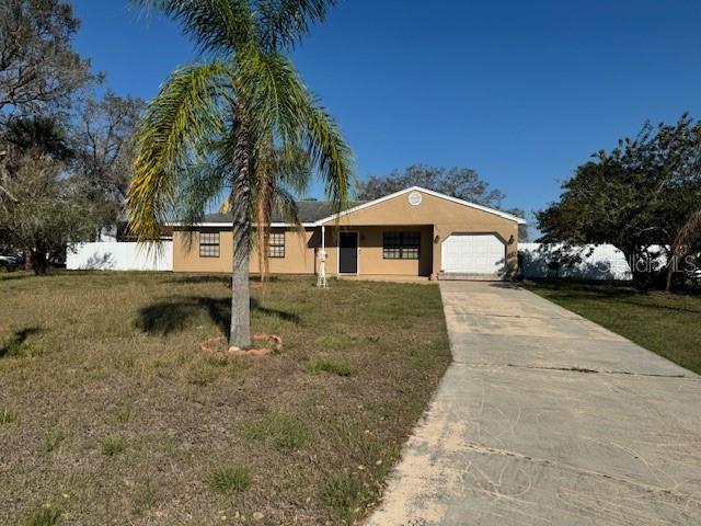 single story home featuring an attached garage, fence, concrete driveway, stucco siding, and a front lawn