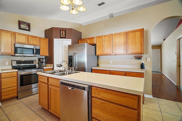 kitchen with vaulted ceiling, sink, light tile patterned floors, stainless steel appliances, and a center island with sink