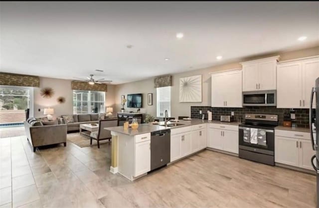 kitchen with stainless steel appliances, open floor plan, white cabinetry, a sink, and a peninsula