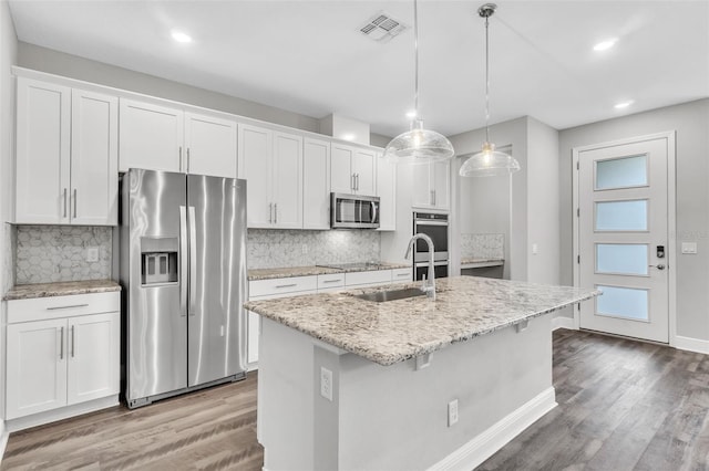 kitchen featuring appliances with stainless steel finishes, decorative light fixtures, an island with sink, and white cabinets