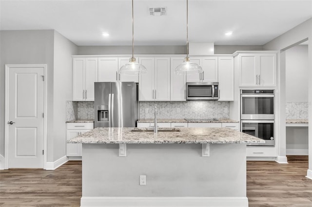 kitchen featuring white cabinetry, a kitchen breakfast bar, hanging light fixtures, a kitchen island with sink, and stainless steel appliances