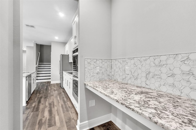 kitchen with appliances with stainless steel finishes, white cabinetry, backsplash, dark hardwood / wood-style flooring, and light stone counters