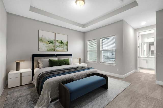 bedroom with a raised ceiling, connected bathroom, sink, and light colored carpet