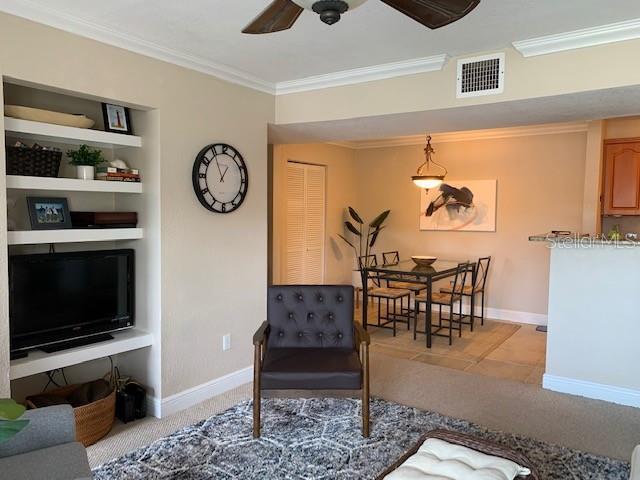 carpeted living room with ceiling fan and ornamental molding