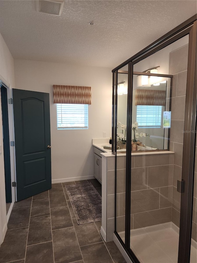 bathroom with visible vents, a stall shower, vanity, a textured ceiling, and baseboards